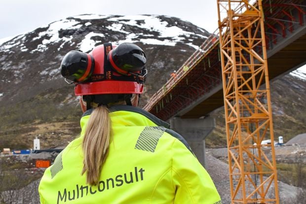 Person i vernetøy som blikker ut over bro og berg